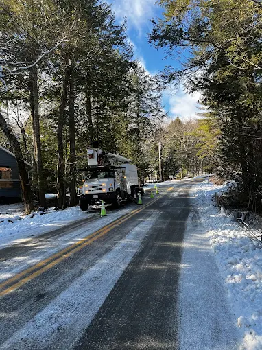 Bucket truck working roadside on a snow-covered street with safety cones set out