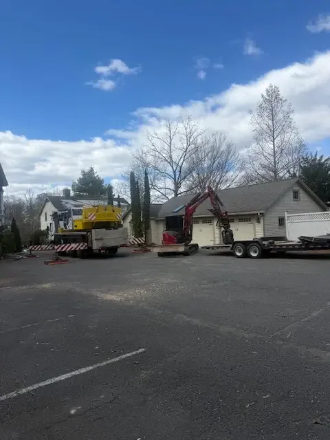 Crane truck and red excavator staged in front of a home for a street-side tree removal