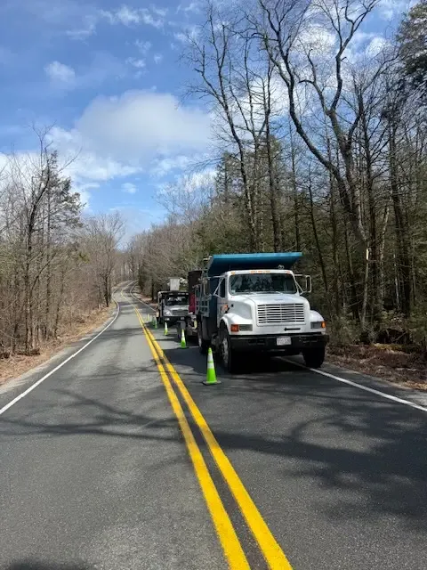 Dump truck and crew vehicles parked along a country road with cones marking the work zone