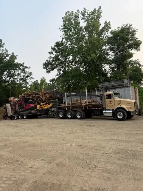 Log truck parked in the yard with its loader boom folded over a stack of timber