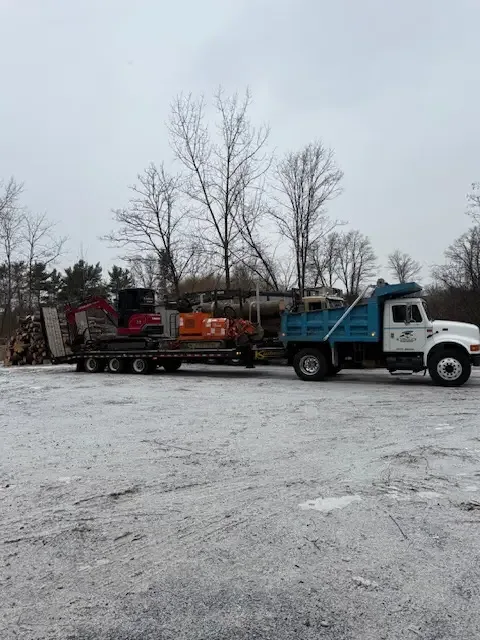 Dump truck, log truck, and equipment trailer lined up in a snowy lot