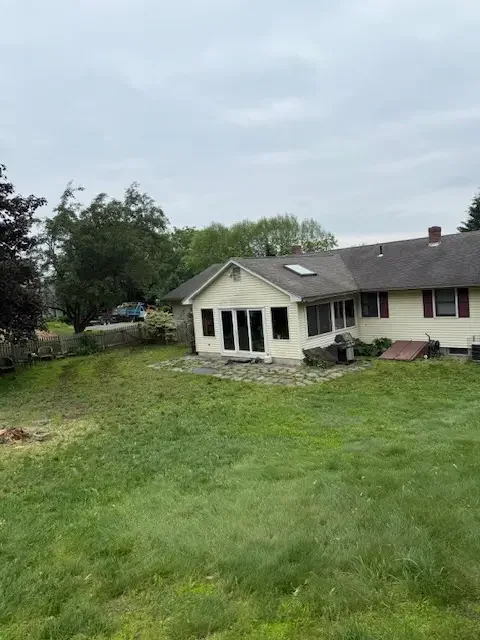 Yellow-sided home with a wide green lawn after tree work on the property