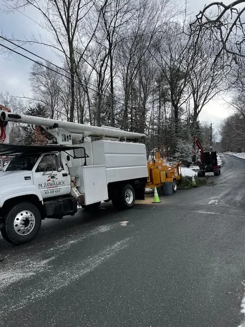 M. Zawalick bucket truck and chipper parked on a wet winter road beside bare trees